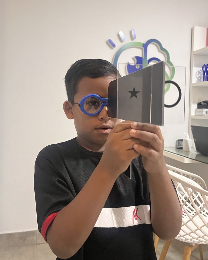 Criança com óculos de prova olhando através de um cartão com uma estrela, durante atendimento